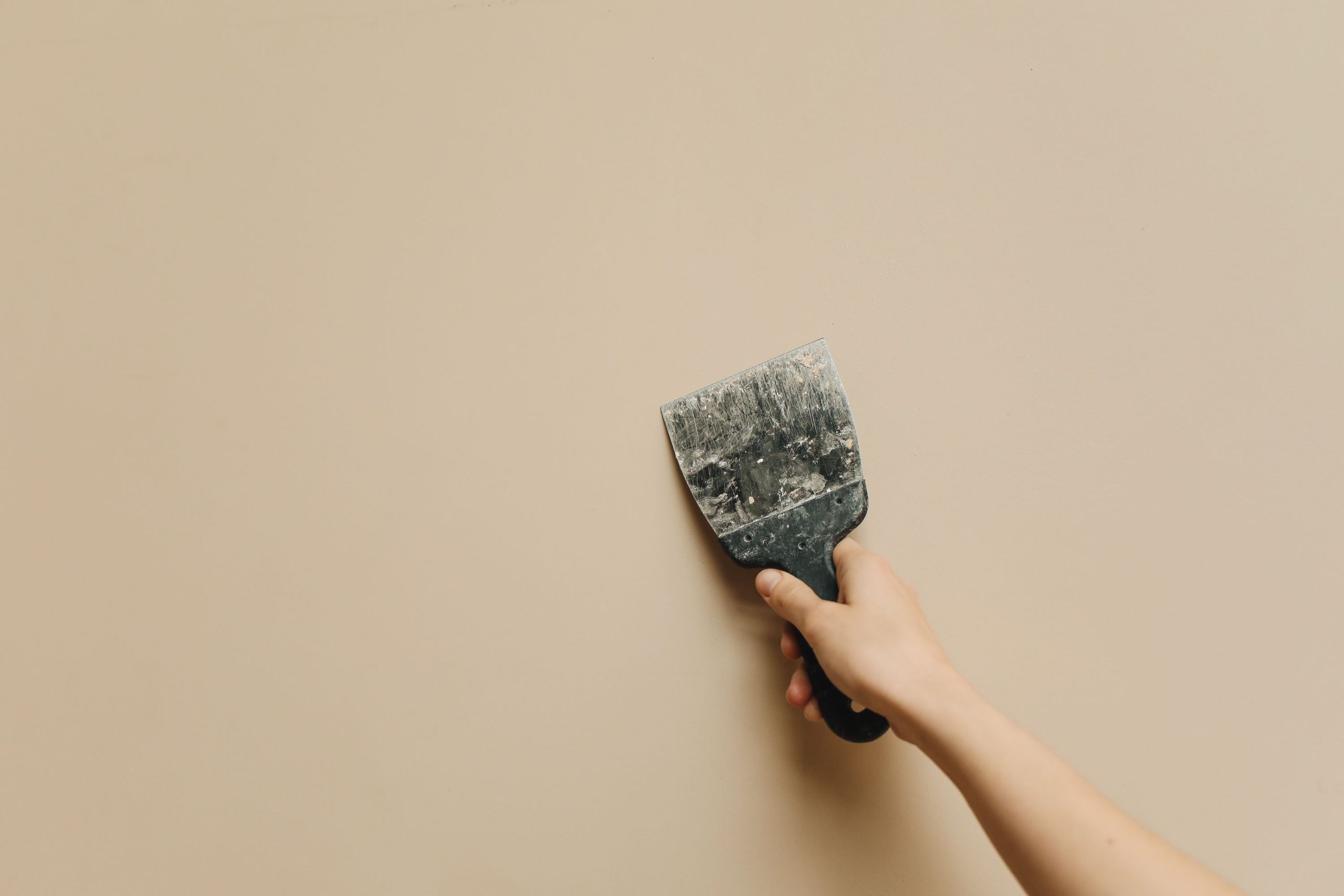 Main tenant spatule contre mur beige rénovation
