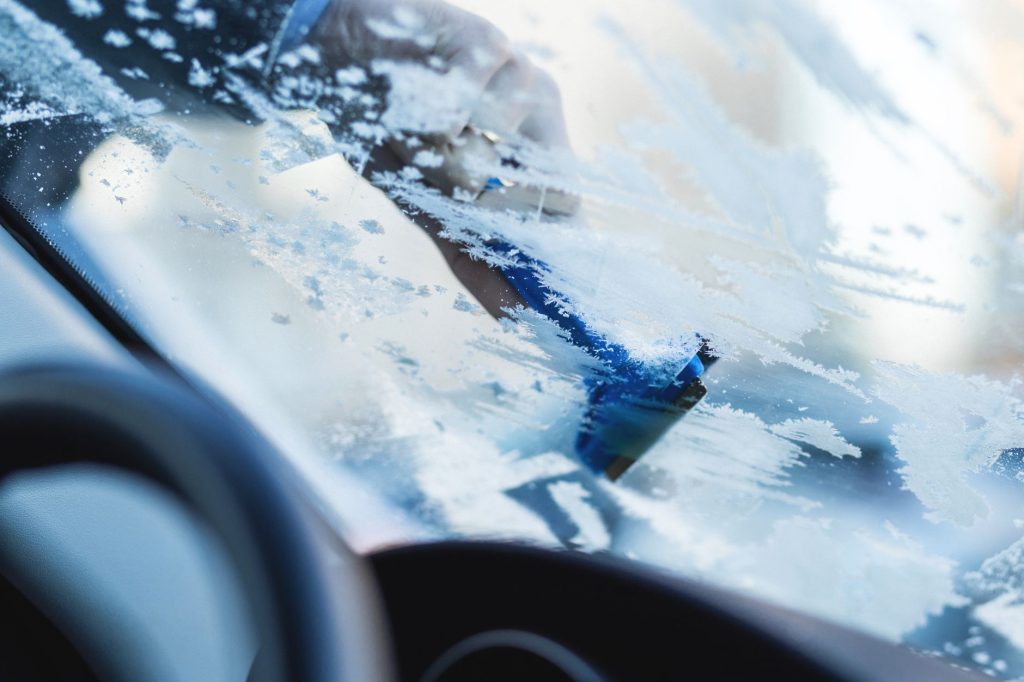 Main gantée raclant la glace du pare-brise