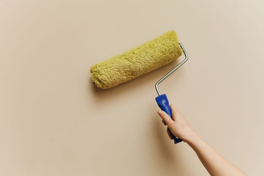 Main appliquant peinture jaune sur mur beige