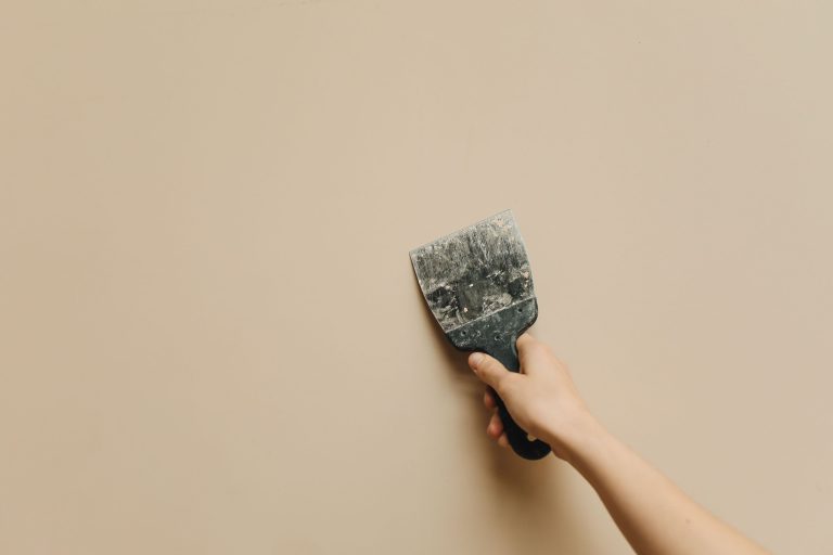 Main tenant une spatule contre mur beige