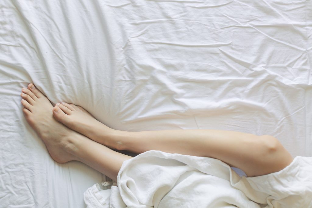 Jambes reposant paisiblement sous des draps blancs